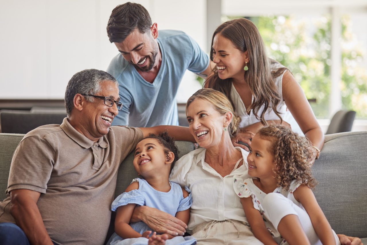 4 adultas e 2 crianças sentadas no sofá sorrindo umas para as outras