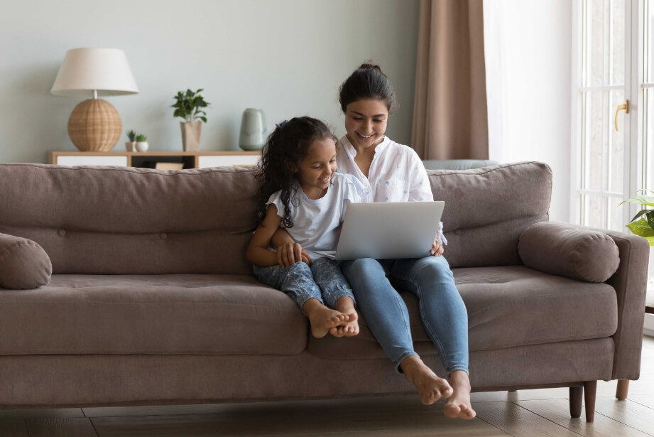 Mãe e filha sentadas no sofá mexendo no computador