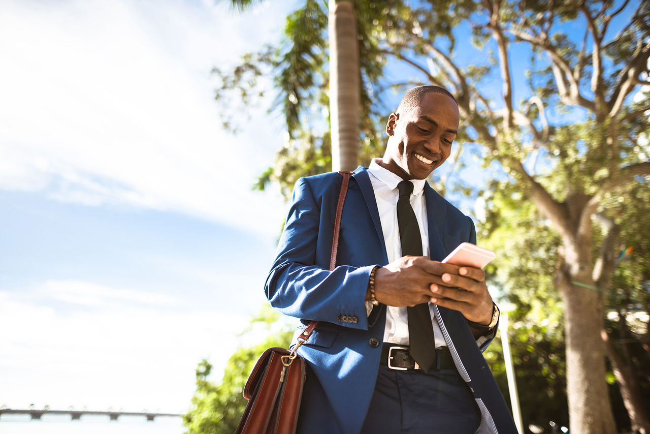 Homem negro usando terno, sorrindo, enquanto digita em smartphone